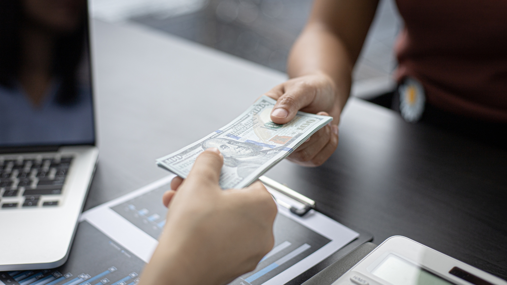 A person holding a bundle of money in front of a laptop